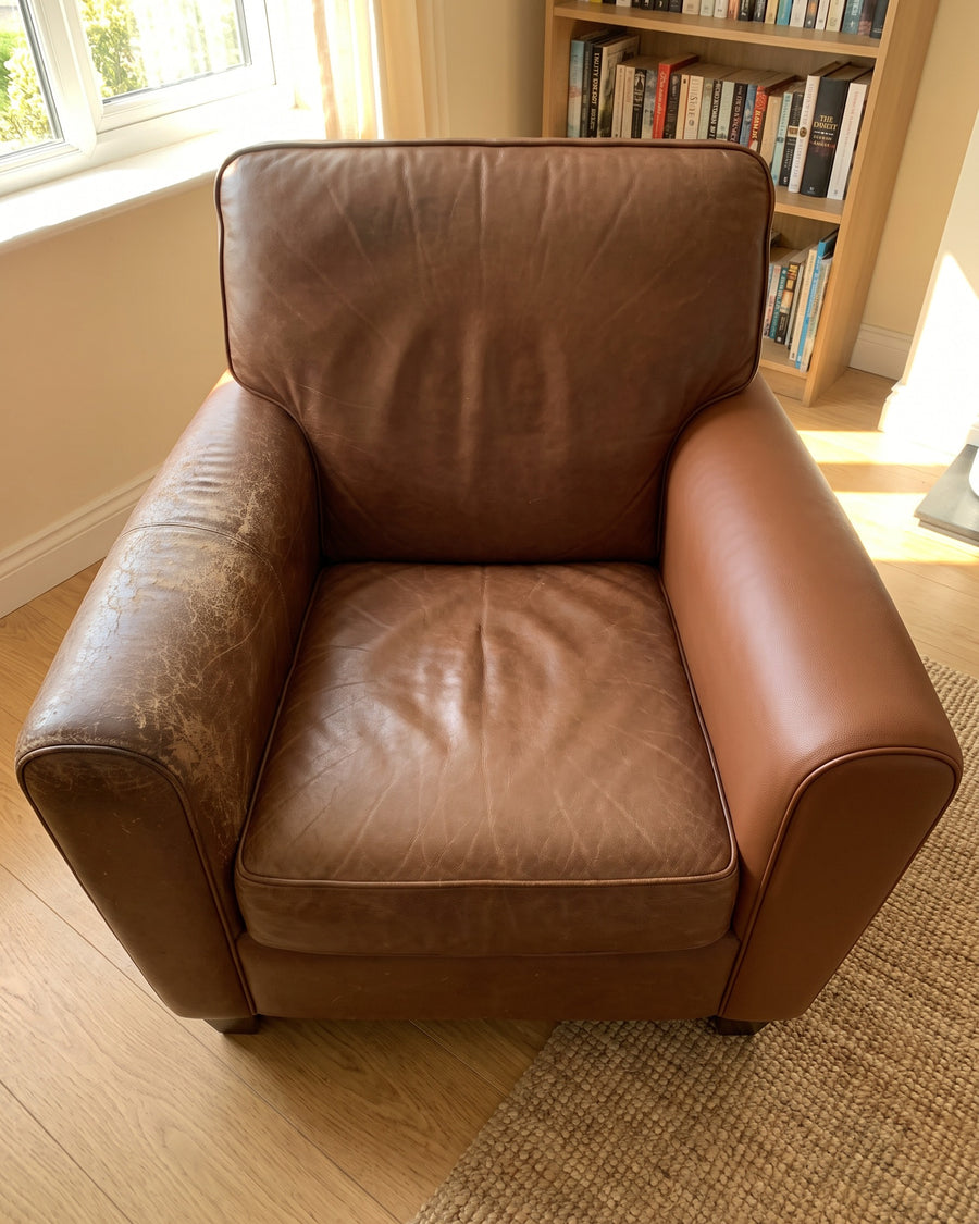 Leren fauteuil met links een versleten armleuning en rechts een opnieuw beklede