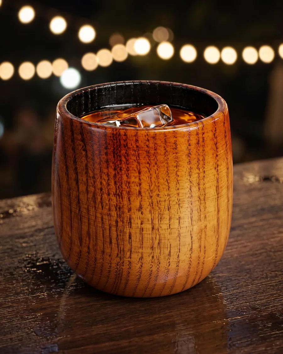 Houten whiskeyglas gevuld met whiskey en een ijsblokje, op een bar in de avond